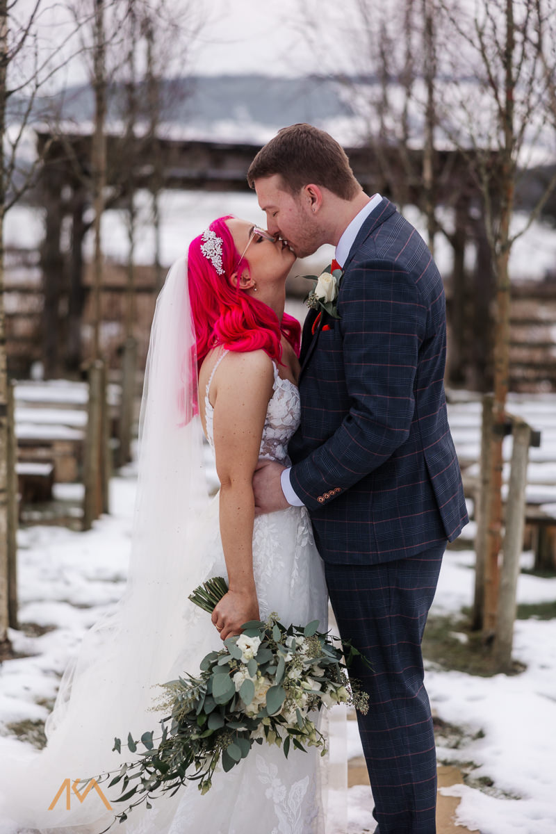 bride groom kissing Bashall Barn wedding venue outside snow gold frosty afternoon 